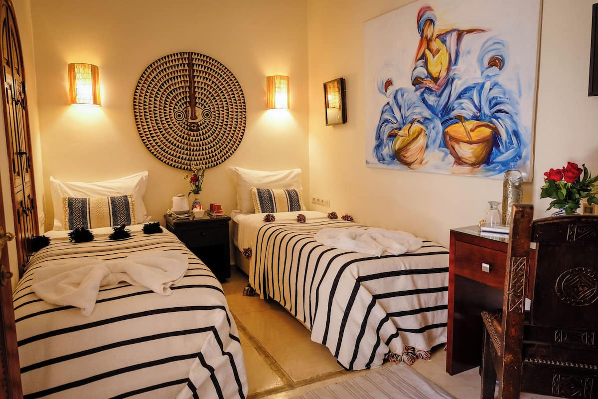 A hotel room with two beds, a large painting, wall sconces, and a wooden dresser.
