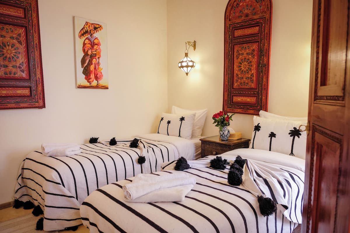 A hotel room with two beds, a nightstand with a vase of flowers, and a wall-mounted light fixture.