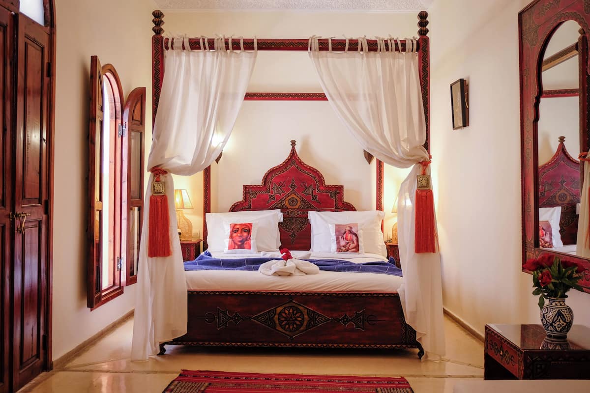 A four-poster bed with a red headboard, white curtains, and a red and white patterned bedspread.