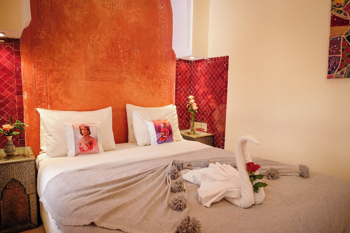 A hotel room with a bed, pillows, a decorative swan, and a vase with flowers.