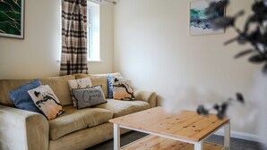 Un salon avec un canapé beige, une table basse en bois, une fenêtre avec des rideaux et un tableau abstrait encadré accroché au mur.