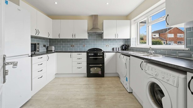 Une cuisine moderne avec des meubles blancs, un four encastré, un lave-linge et une fenêtre donnant sur un quartier résidentiel.