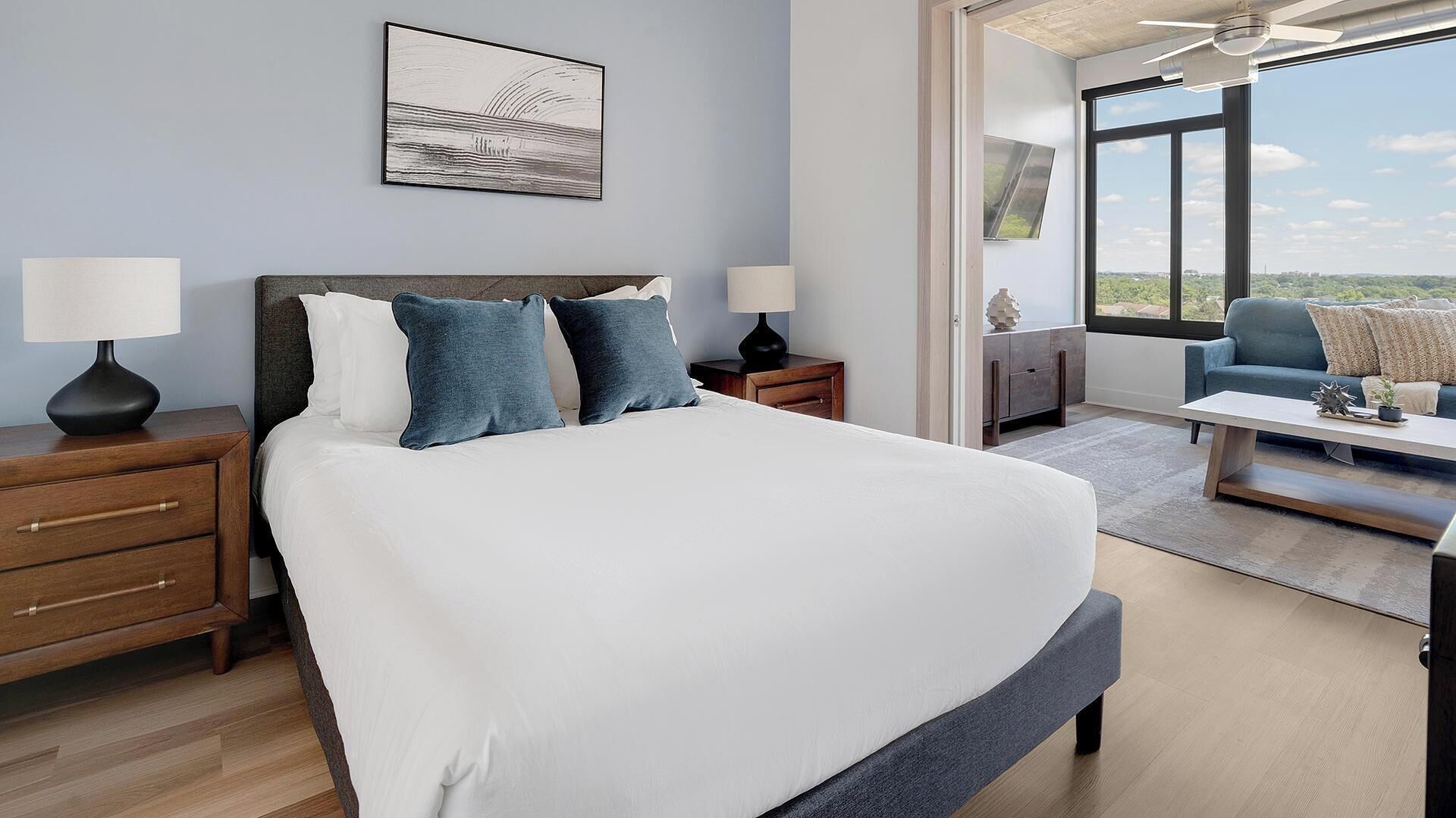 A modern hotel room with a large bed, bedside tables, a desk, and a view of the outdoors.