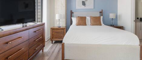 A bedroom with a bed, wooden dresser, nightstands, a television, and a wall-mounted artwork.