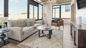 Una sala de estar moderna con sofá, sillón, mesa de centro y vistas de la ciudad a través de amplias ventanas.
