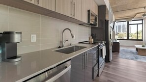 A modern kitchen with a built-in dishwasher, stainless steel appliances, and a window providing a view of the city. - Landing | Stunning 2BD, Gym, Game Room (Arlington)
