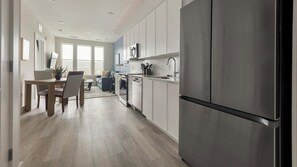 A modern kitchen with a stainless steel refrigerator, wooden dining table, and light-colored cabinetry. - Landing | Incredible 1BD in Columbia Heights (Washington)