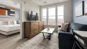 A modern bedroom with a bed, dresser, TV, and a view of buildings through large windows. - Landing | Incredible 1BD in Columbia Heights (Washington)