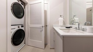Un baño moderno con un lavamanos blanco, un espejo y dos lavadoras apiladas.