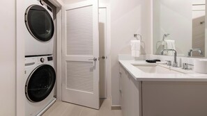 Ein modernes Badezimmer mit Waschbecken, Spiegel und zwei übereinander angeordneten Waschmaschinen.