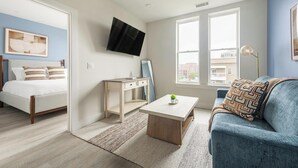 Un dormitorio moderno con cama, escritorio, mesa de centro y televisor montado en la pared.