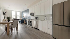Una cocina moderna con armarios blancos, electrodomésticos de acero inoxidable y un comedor con mesa y sillas de madera.