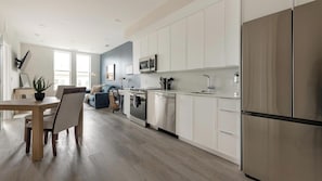 Eine moderne Küche mit weißen Schränken, Edelstahlgeräten und einem Essbereich mit Holztisch und Stühlen.