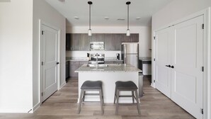 A modern kitchen with granite countertops, stainless steel appliances, and a central island with bar stools. - Landing | Chic 2BD, Gym (Knoxville)