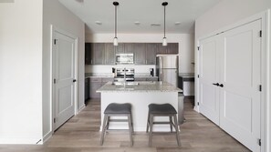 A modern kitchen with granite countertops, stainless steel appliances, and a central island with bar stools. - Landing | Spectacular 2BD, Gym (Knoxville)