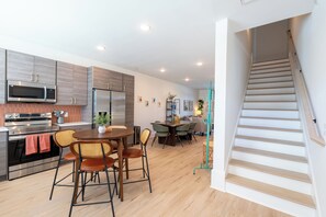 Eine moderne Küche mit integrierten Geräten, ein Essbereich mit rundem Tisch und Stühlen sowie eine Treppe, die zu einer oberen Etage führt.