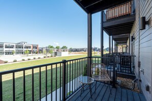 Ein Balkon mit Gartenmöbeln, freier Blick auf ein Sportfeld und ein modernes Gebäude im Hintergrund.
