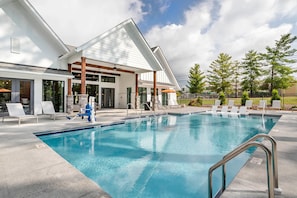 Ein Swimmingpool mit Liegestühlen und einem überdachten Bereich, umgeben von einem Gebäude mit großen Fenstern und einer Steinsäule.
