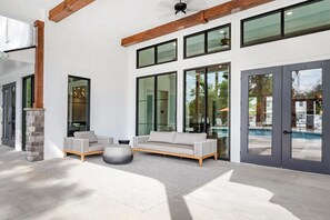 Ein moderner Außenbereich mit einer Sitzecke, bestehend aus einer Couch und Stühlen, einer Steinpfeiler und Blick auf einen Swimmingpool durch große Glasfenster.