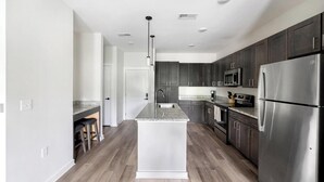 Una cocina moderna con gabinetes oscuros, electrodomésticos de acero inoxidable y una encimera de granito.
