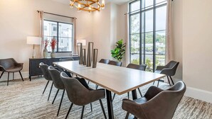 Een moderne eetruimte met een grote tafel, meerdere stoelen, een kroonluchter en uitzicht door grote ramen.