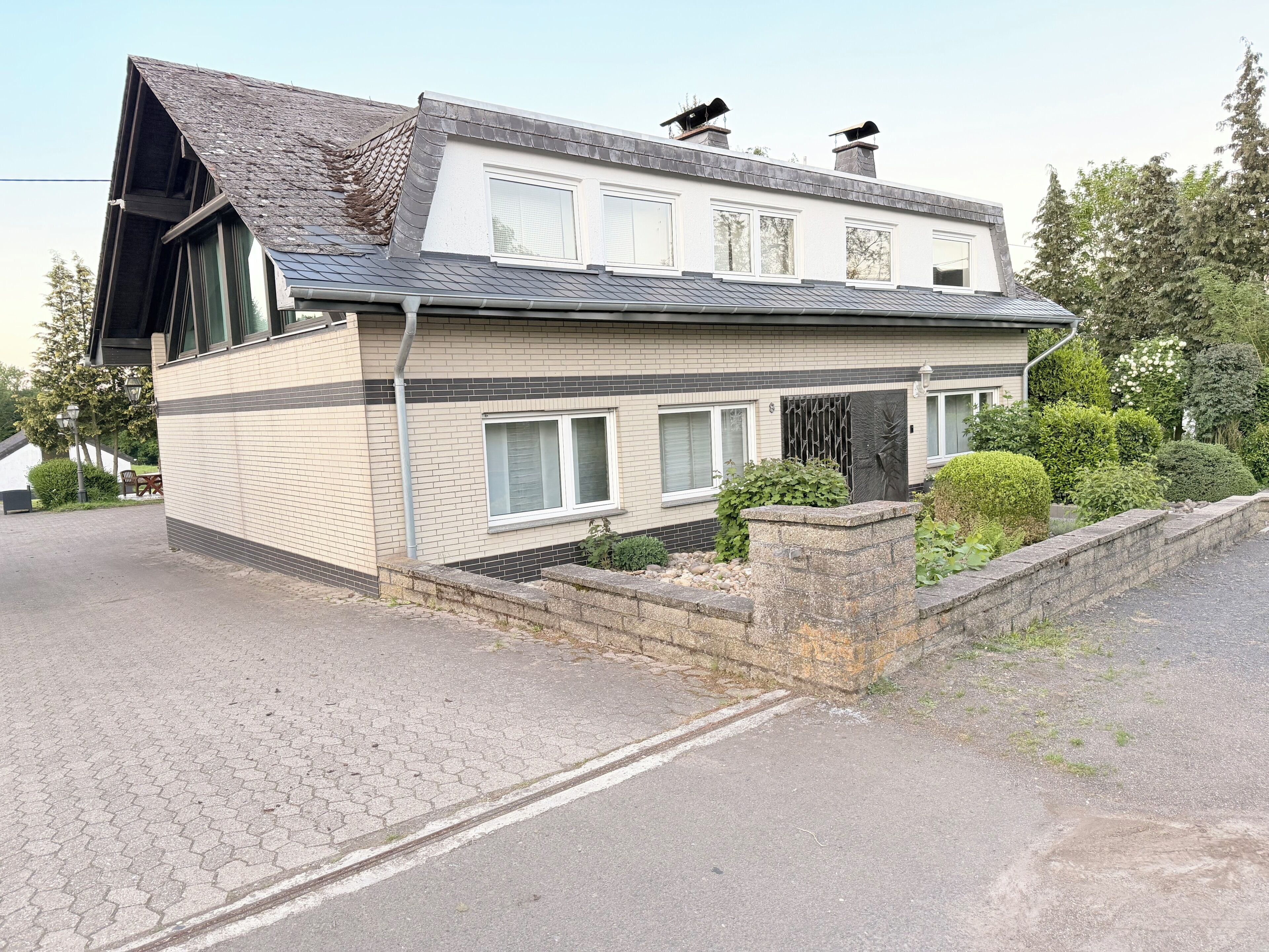 Une maison à deux étages, dotée d’un toit en pente, de grandes fenêtres et d’un mur de soutènement en pierre.