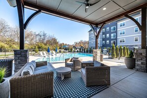 A covered outdoor area with a pool, wicker furniture, and a view of a multi-story building. - Landing | Modern 2BD, Gym (Knoxville)