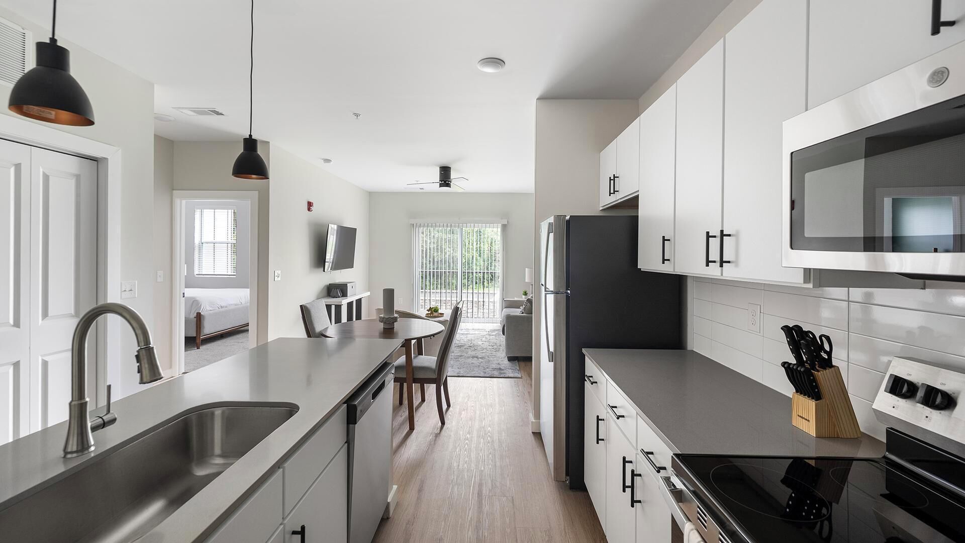 Een moderne keuken met roestvrijstalen apparatuur, een eethoek met een tafel en stoelen, en uitzicht op een balkon.