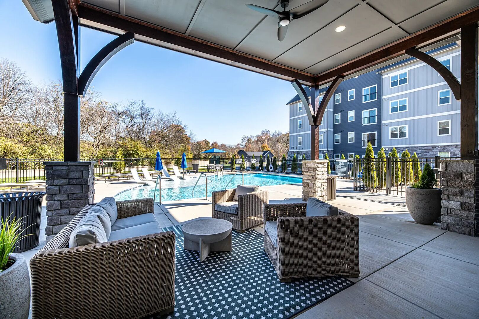 A covered outdoor area with a pool, wicker furniture, and a view of a multi-story building.