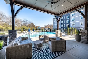 A covered outdoor area with a pool, wicker furniture, and a view of a multi-story building. - Landing | Stylish 1BD, Gym (Knoxville)