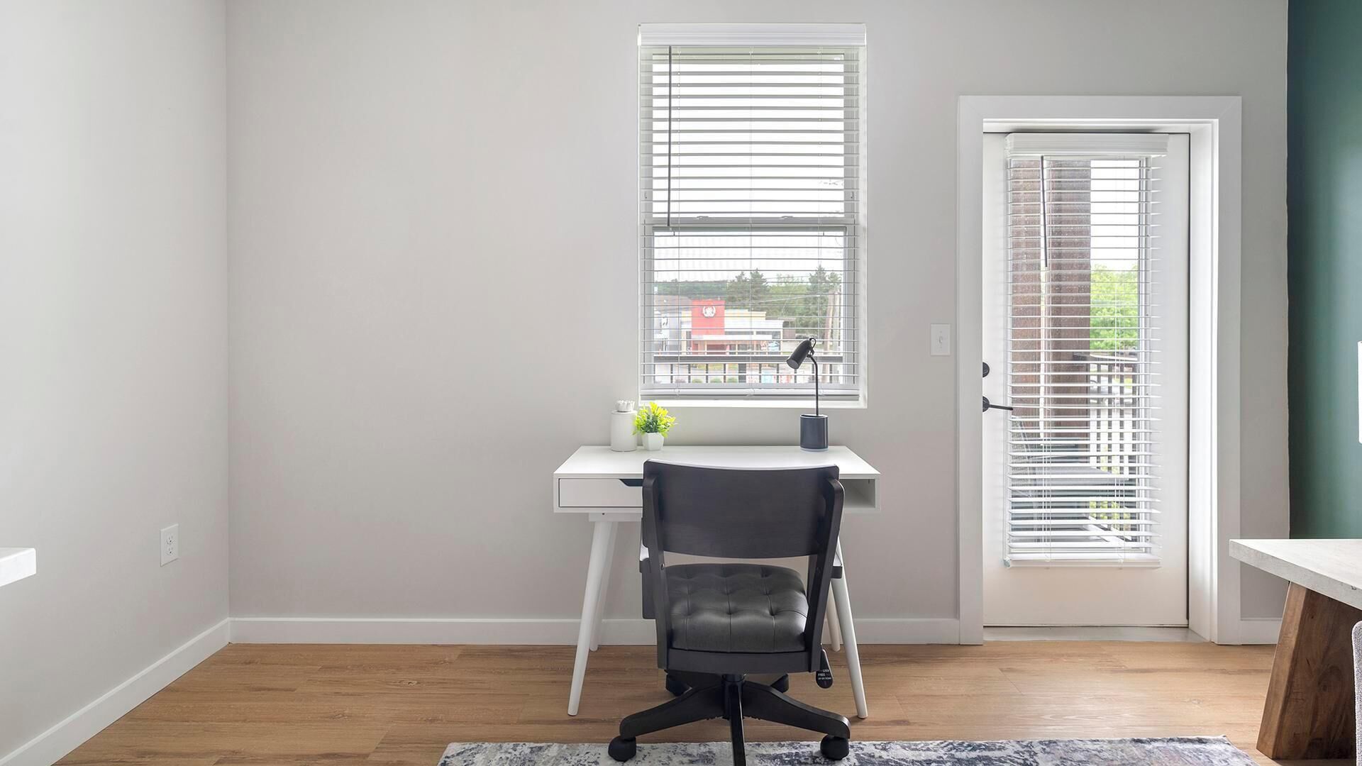 A room with a desk, chair, and a door with blinds.