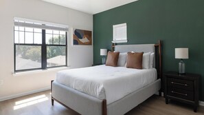 Une chambre à coucher avec un lit, des tables de chevet, une fenêtre et des œuvres d’art accrochées au mur.