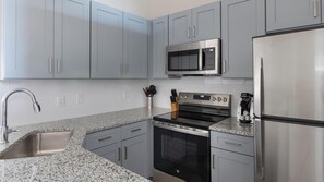 Une cuisine moderne avec des meubles gris, des appareils en acier inoxydable et un plan de travail en granit.