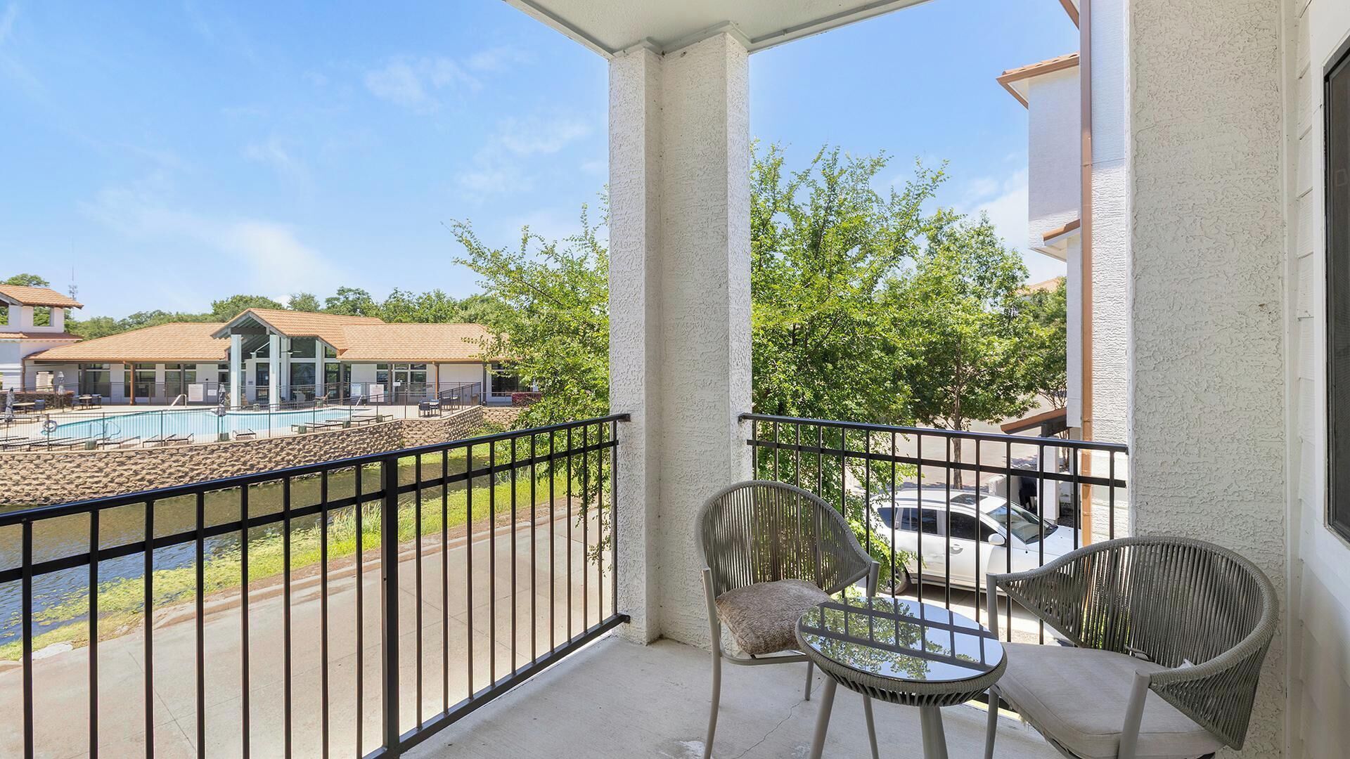 A balcony with a view of a swimming pool, a building, and trees.