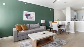 Ein modernes Wohnzimmer mit einem grauen Sofa, einem Couchtisch und einem Essbereich mit Stühlen und einem Tisch.