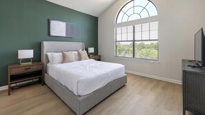 A bedroom with a bed, nightstands, a lamp, a TV, a window with blinds, and a painting on the wall. - Landing | Spectacular 2BD, Gym (Garland)