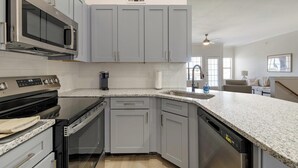 A kitchen with grey cabinets, a built-in microwave, a dishwasher, and a granite countertop. - Landing | Stylish 2BD, Gym (Garland)