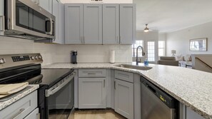 A kitchen with grey cabinets, a built-in microwave, a dishwasher, and a granite countertop. - Landing | Spectacular 2BD, Gym (Garland)