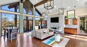A spacious living area with a large sofa, dining table, and chairs, a kitchen with wooden cabinets, and a balcony with large windows. - Landing | Stylish 2BD, Gym (Garland)