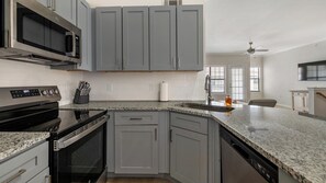 A kitchen with grey cabinets, a black microwave, a stainless steel range hood, and a granite countertop. - Landing | Chic 2BD, Gym (Garland)