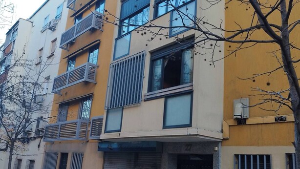 A multi-story building with balconies, a closed shuttered storefront, and a tree in the foreground. - Room-cozy Guest Room in Modern Madrid Fl (Madrid)