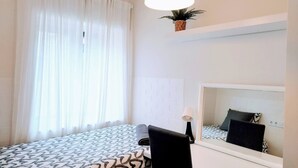 A hotel room with a bed, a desk, a chair, a large mirror, and a window with curtains. - Room-cozy Guest Room in Modern Madrid Fl (Madrid)