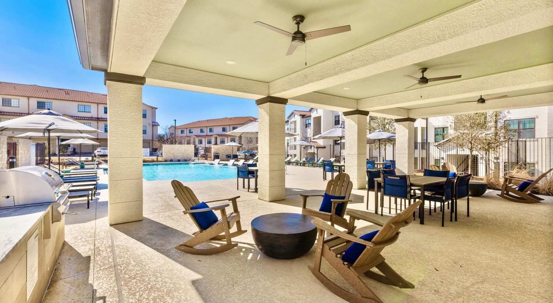 A covered outdoor area with seating, a barbecue grill, and a pool in the background.