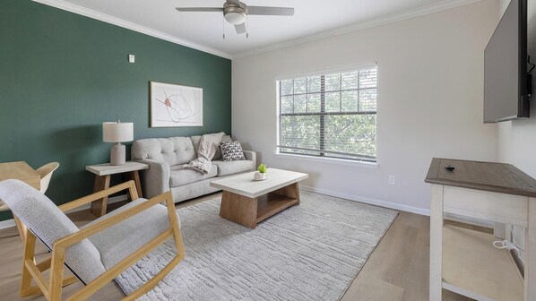 A living room with a sofa, coffee table, and a TV mounted on the wall. - Landing | Spectacular 2BD, Gym (Garland)