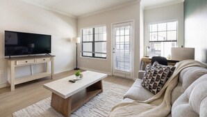A living room with a TV, a desk, a coffee table, and a sofa. - Landing | Spectacular 2BD, Gym (Garland)
