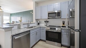 A modern kitchen with stainless steel appliances, grey cabinets, and a granite countertop. - Landing | Spectacular 2BD, Gym (Garland)