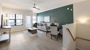 A modern living room with a sofa, coffee table, and dining area. - Landing | Spectacular 2BD, Gym (Garland)