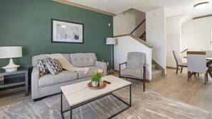 Een woonkamer met een bank, fauteuil, salontafel en een trap die naar een ander niveau leidt.