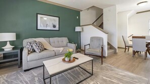 A living room with a sofa, armchair, coffee table, and a staircase leading to another level. - Landing | Stylish 2BD, Gym (Garland)