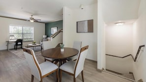 A dining area with a round table, four chairs, a ceiling fan, a staircase, and a window with blinds. - Landing | Stylish 2BD, Gym (Garland)